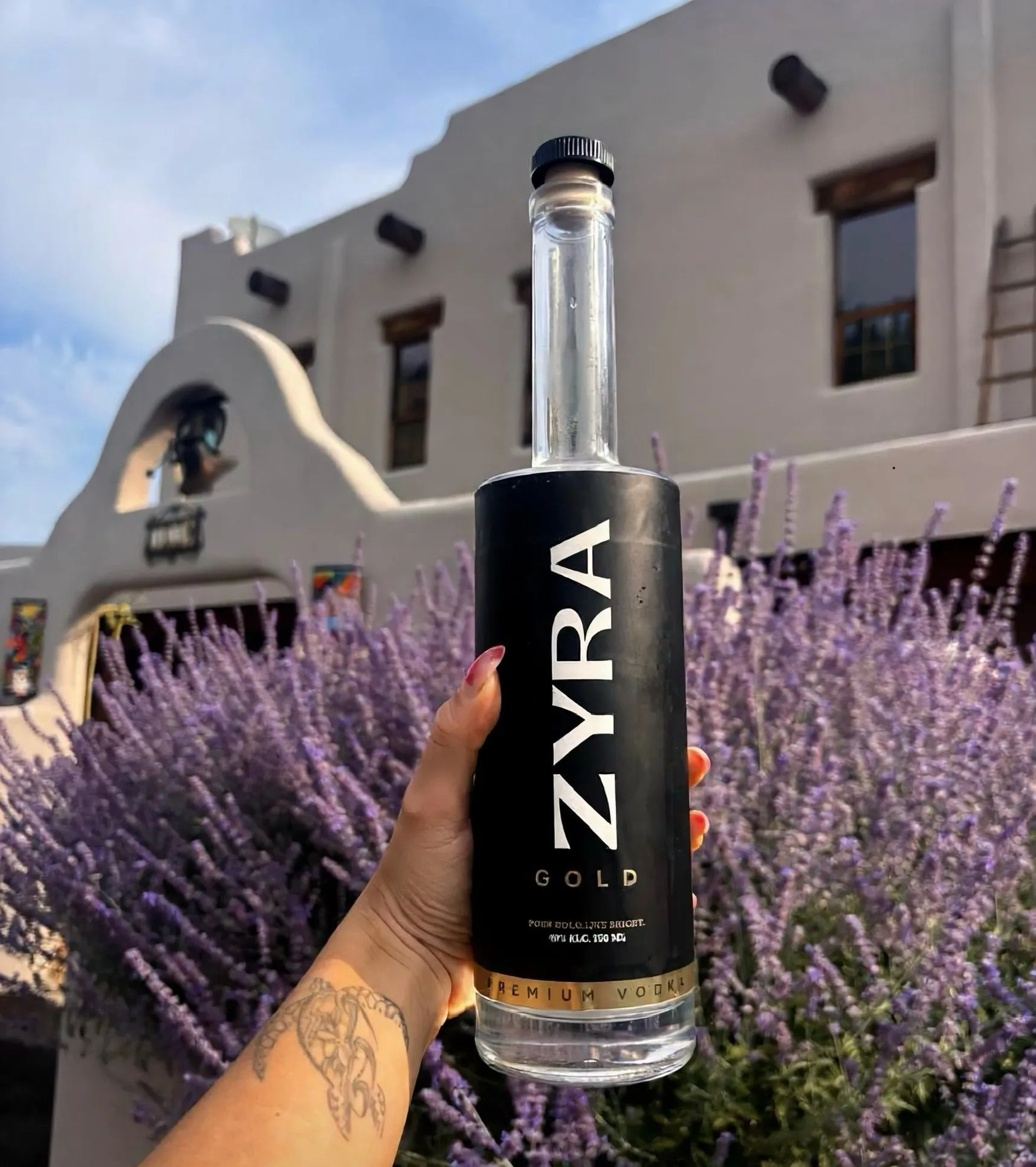 Zyra Gold vodka held up in front of a lavender garden and adobe building